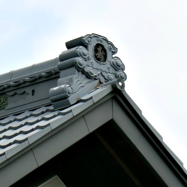 A carved stone roof finial rides the ridge of a house in Japan.  These were usually decorated with the crest of the family.