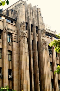 Art Deco building in Mumbai, India with two elongated statues flanking the door.  They are armed and dangerous.