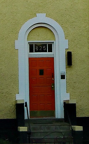 The door is unusually narrow.  The white, sthone frame helps the door seem appropriately sized for the house.